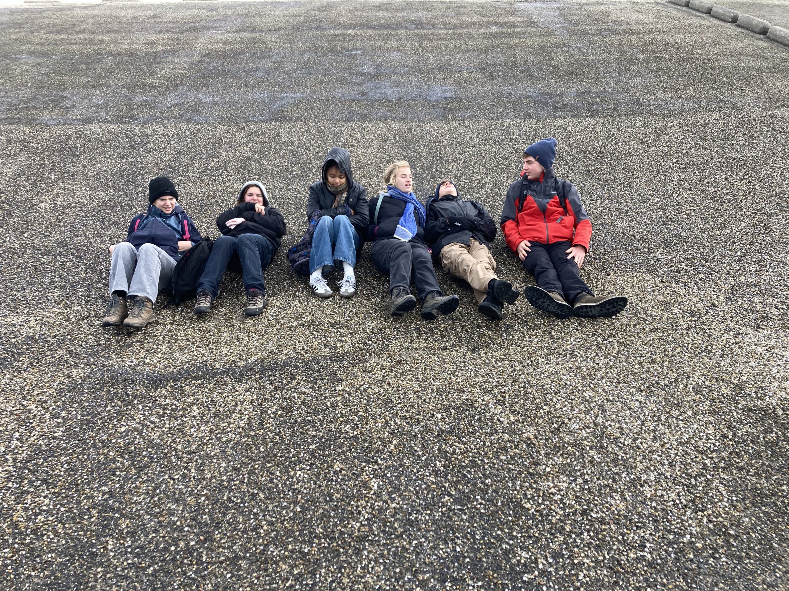 Maud Vanhauwaert en Frederik Neyrinck gingen voor de productie 'In What We Trust' drie dagen lang door weer en wind op stap met zes jongeren en spraken over waar zij in geloven. Jongeren uit productie 'In What We Trust' liggen op asfalt.