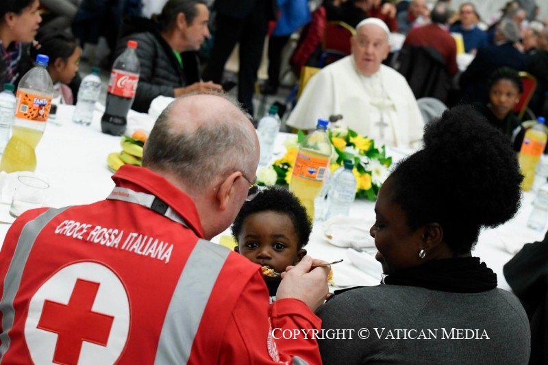 Solidariteit haalt mensen aan de rand van de samenleving uit de onzichtbaarheid. Een man van het Rode Kruis lepelt de maaltijd op aan een baby. Op de achtergrond een glunderende paus aan dezelfde tafel.