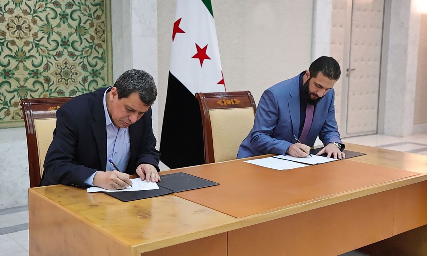 Koerdisch militair leider Mazloum Abdi en Syrisch interimpresident Ahmed al-Sharaa tekenen de intentieverklaring. Koerdisch militair leider Mazloum Abdi en Syrisch interimpresident Ahmed al-Sharaa tekenen de intentieverklaring.