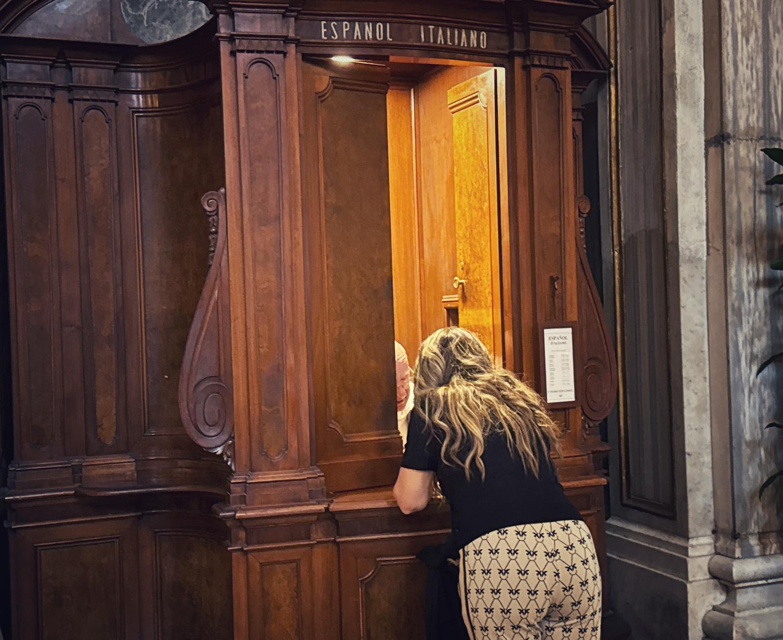 Een vrouw is aan het biechten, staat voorover gebogen te praten met een priester in de biechtstoel in Santa Maria Maggiore.