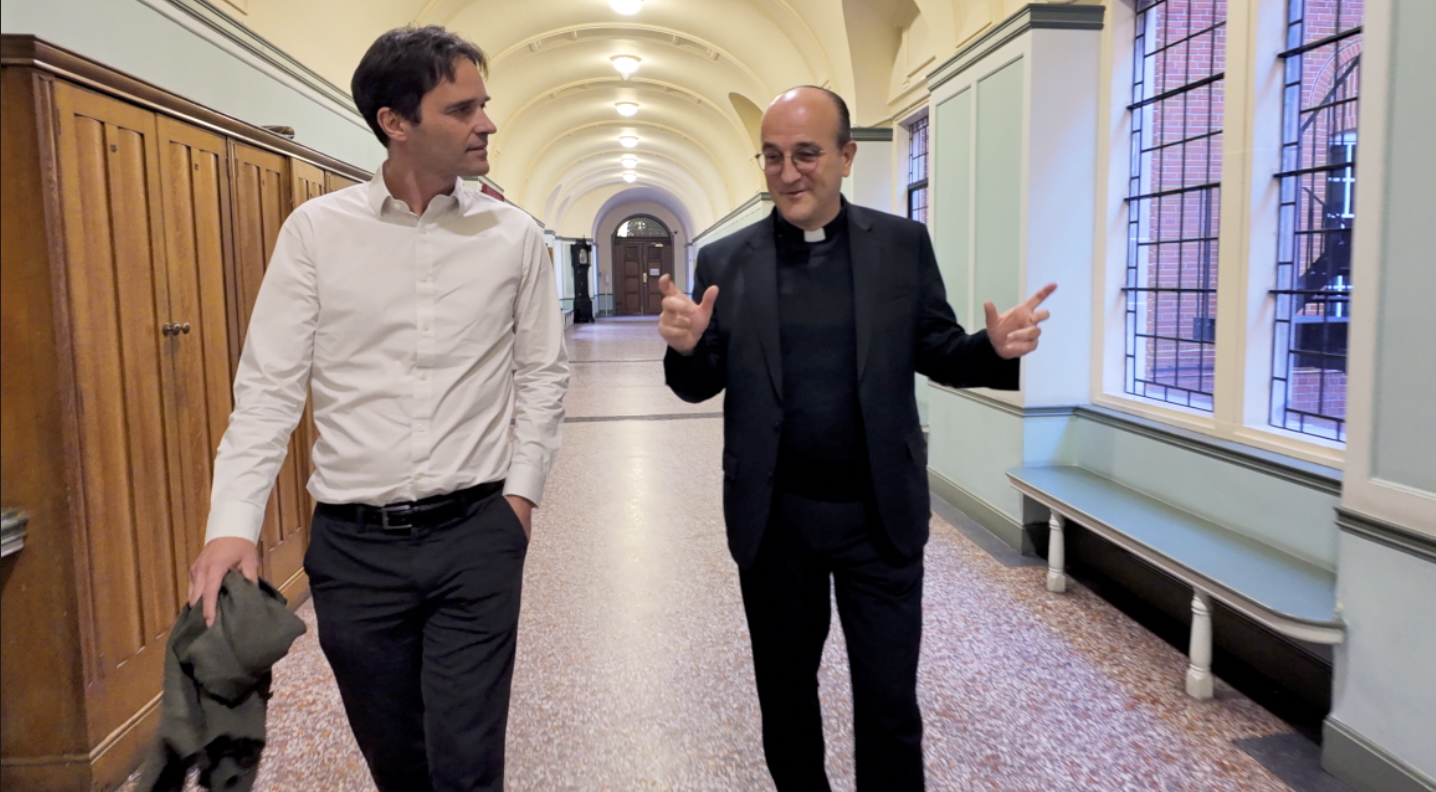 Patrick van der Vorst werd na een leven als kunstschatter tot priester gewijd in 2023. Patrick van der Vorst loopt met Koen Vlaeminck door een gang.