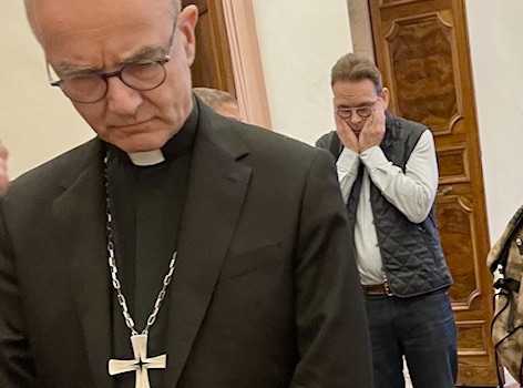 Lieve Brouwers fotografeert een aangeslagen bisschop Thibault Verny tijdens pauze. Thibault Verny, hoofd gebogen, tijdens pauze. Daarachter Koen Van Sumeren met hoofd in de handen. Duidelijk zwaar gesprek geweest.