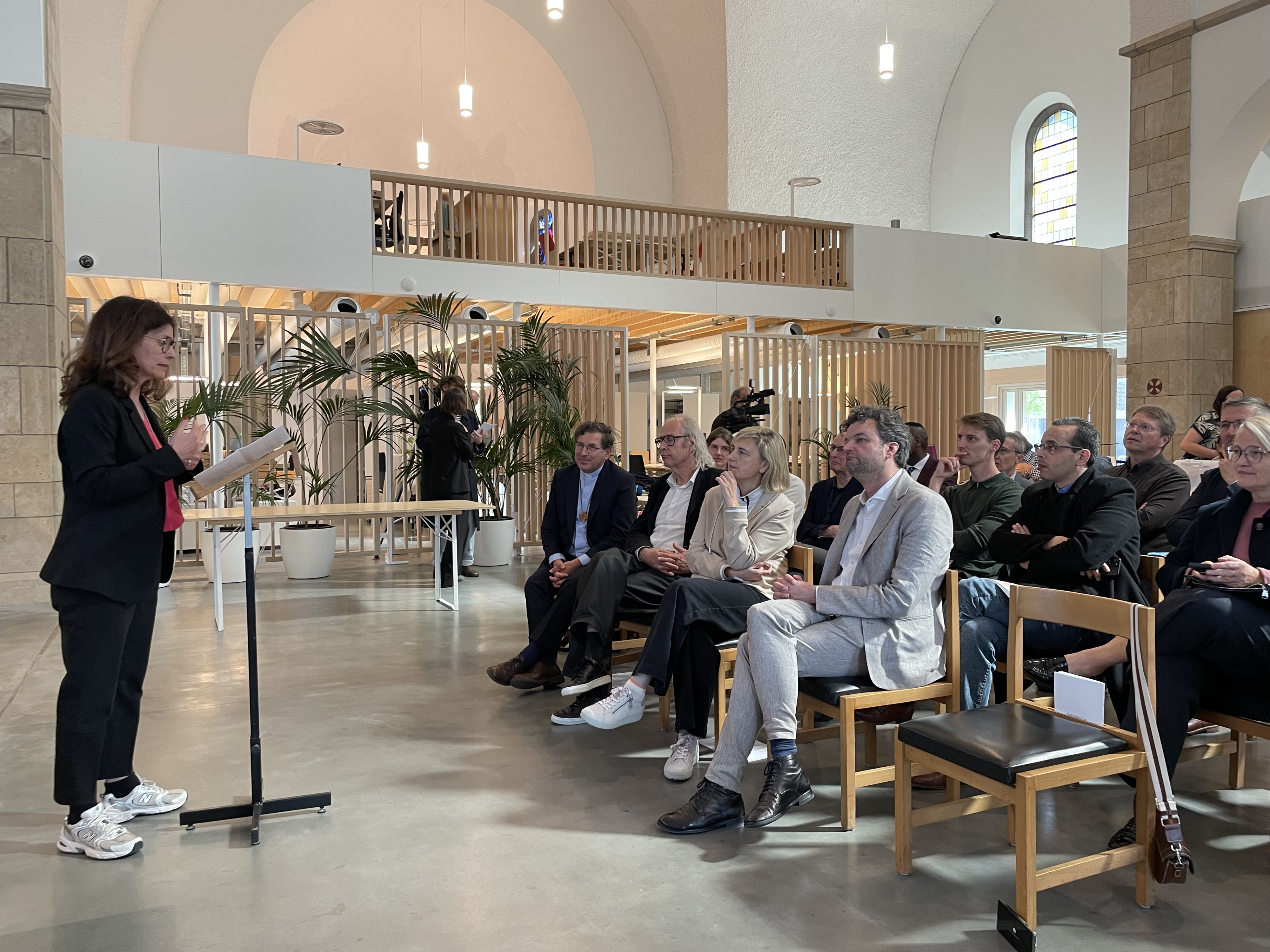 Nathalie Debast van VVSG spreekt het publiek toe, met vooraan minister Crevits en bisschop Lode Aerts.