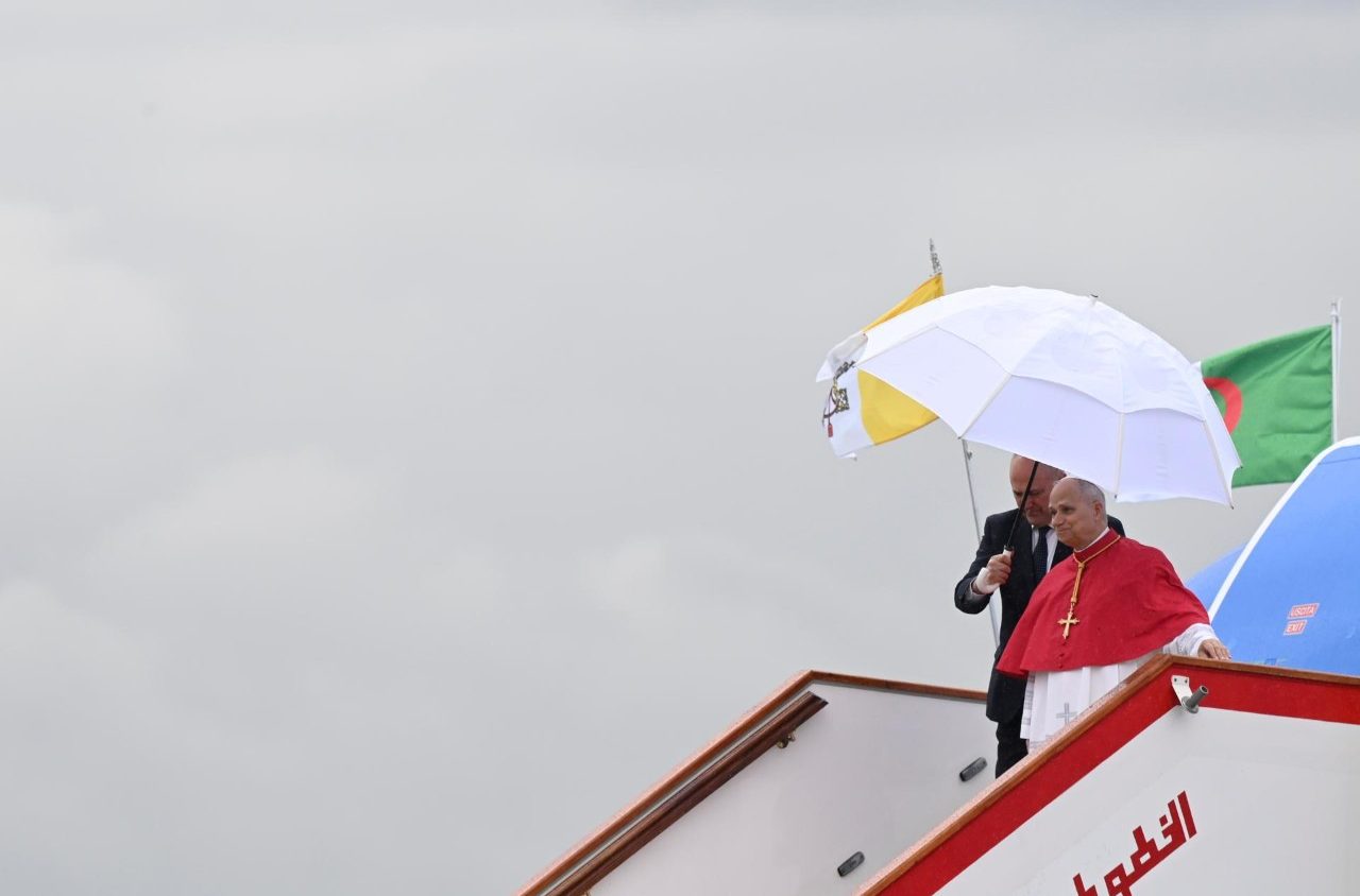 Paus Leo XIV komt aan in een regenachtig Algerije, waar hij Sint-Augustinus wil eren als brugfiguur. Paus Leo XIV stapt uit het vliegtuig met een witte paraplu.