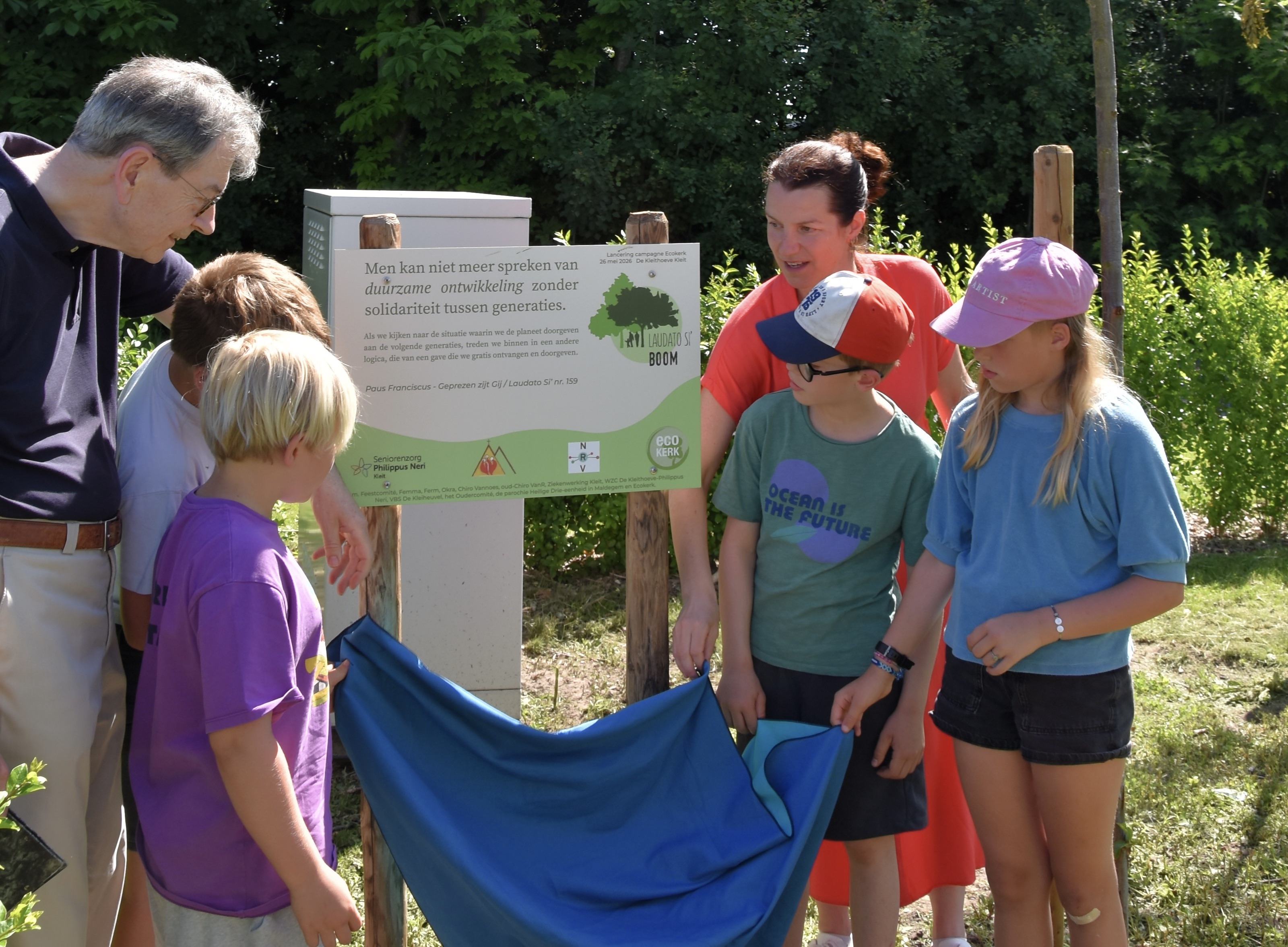 Albert Verleyen en Katrijn Ruebens, directeur van wzc De Kleithoeve in Maldegem, onthullen het Laudato si-bord samen met kinderen van de basisschool. 