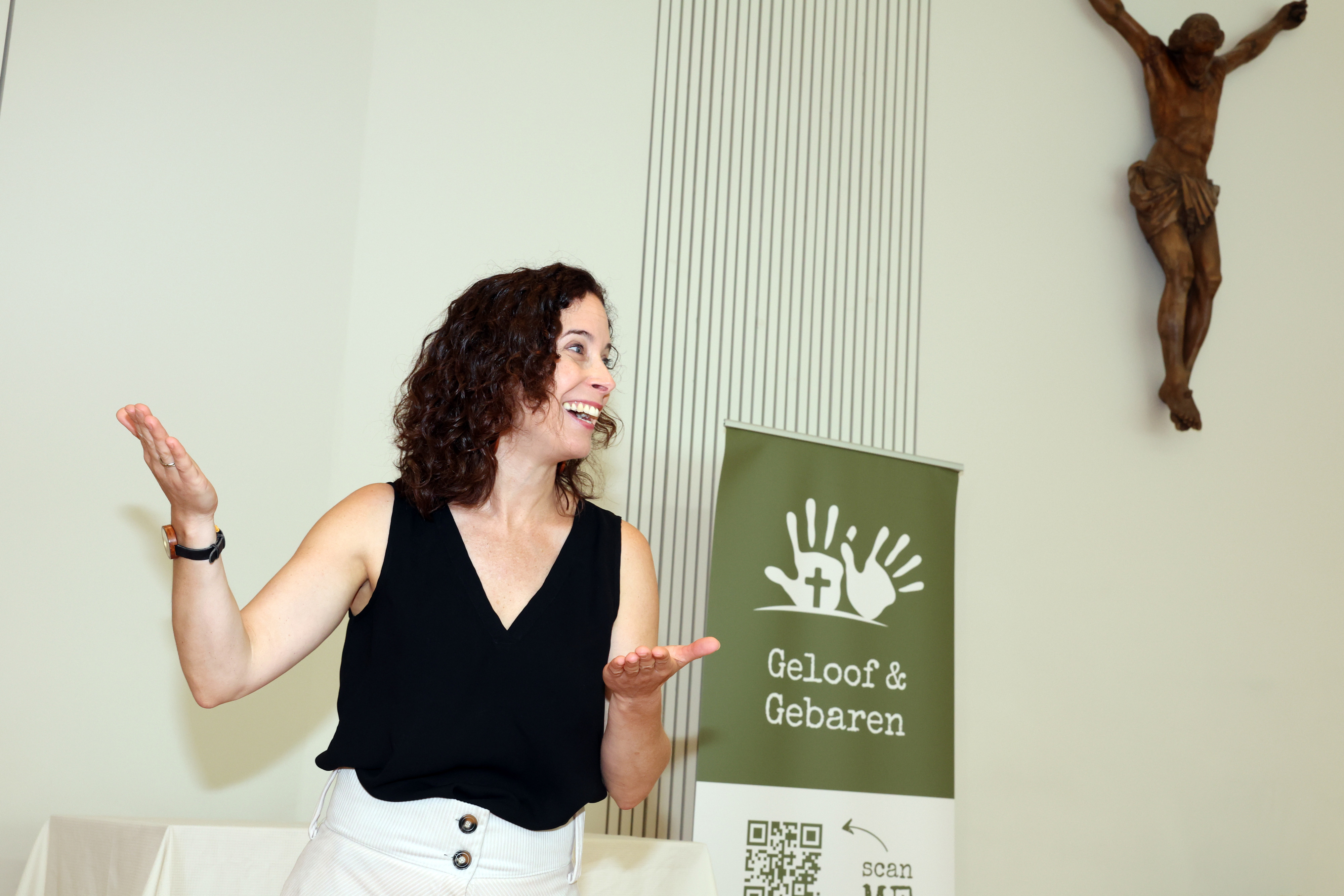 Janneke Verduijn, initiatiefnemer van Geloof & Gebaren, met grote smile op gezicht druk aan het tolken voor een banner van haar organisatie.