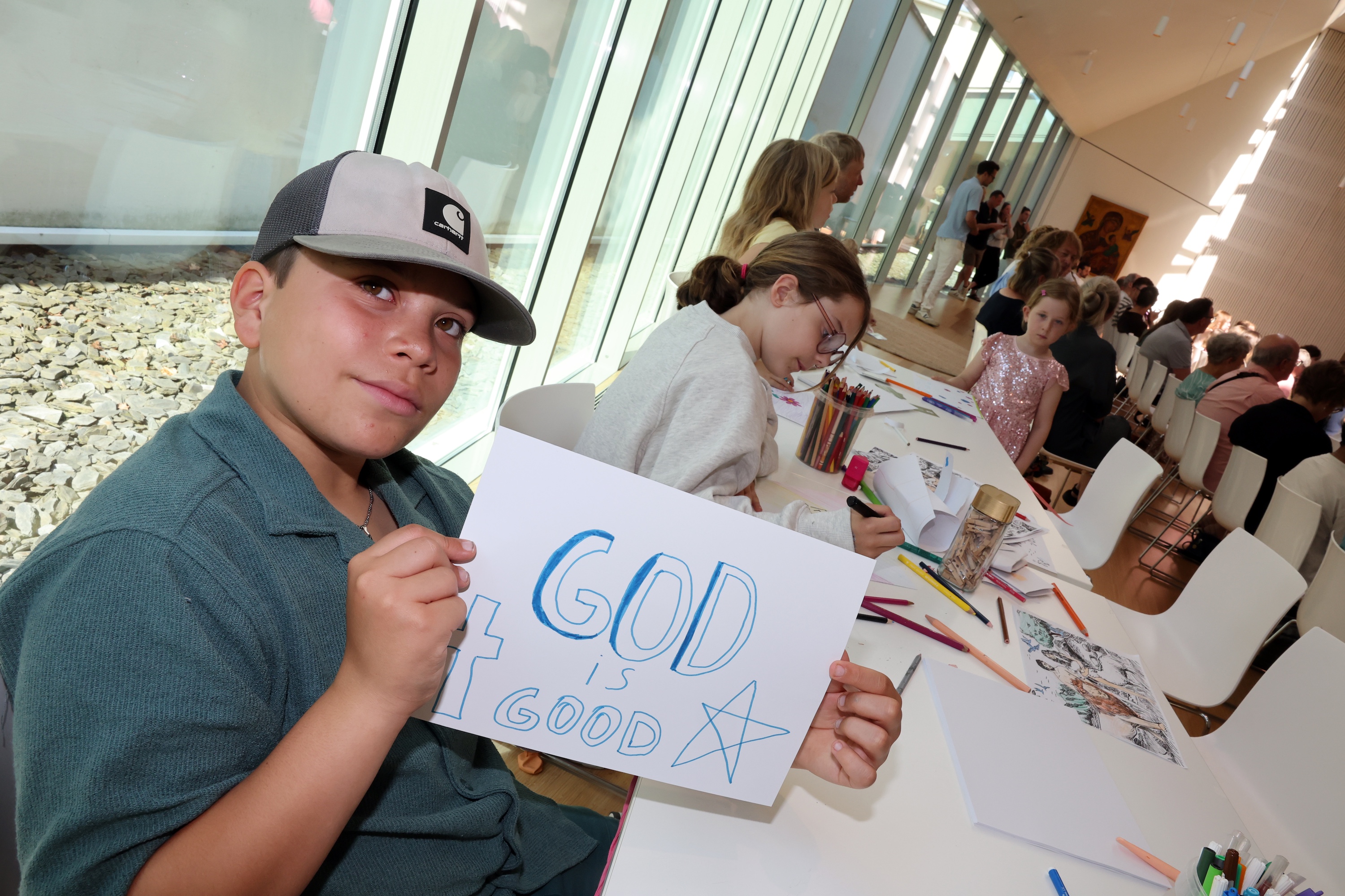 Een kind toont een tekening waarop staat (in het Engels): 'God is good.'