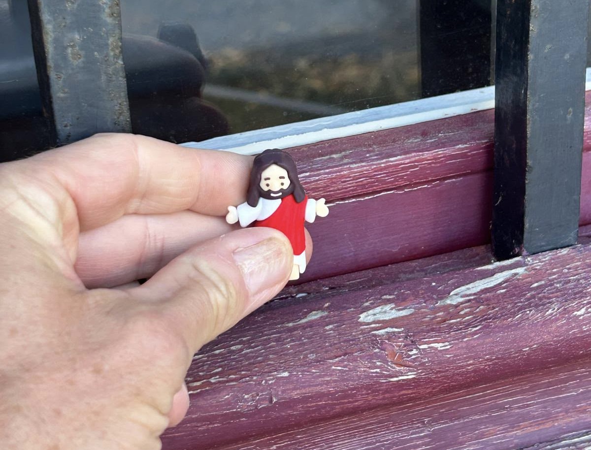 Een hand steekt een Jezus poppetje ergens tussen.