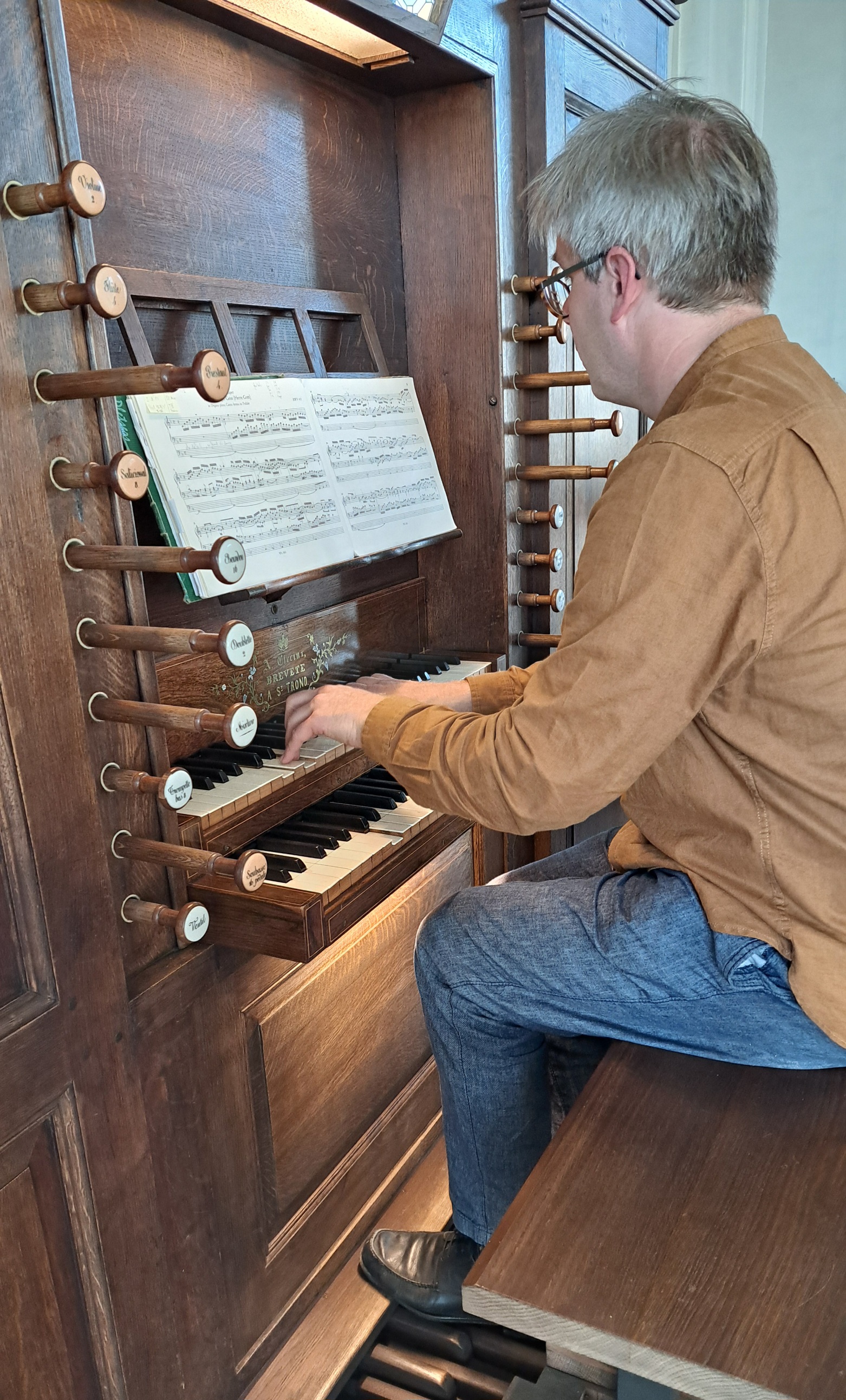 Bruno Bruyninckx die op het pijporgel (een kerkorgel) speelt, waarbij de speeltafel met klavieren en registers zichtbaar is.