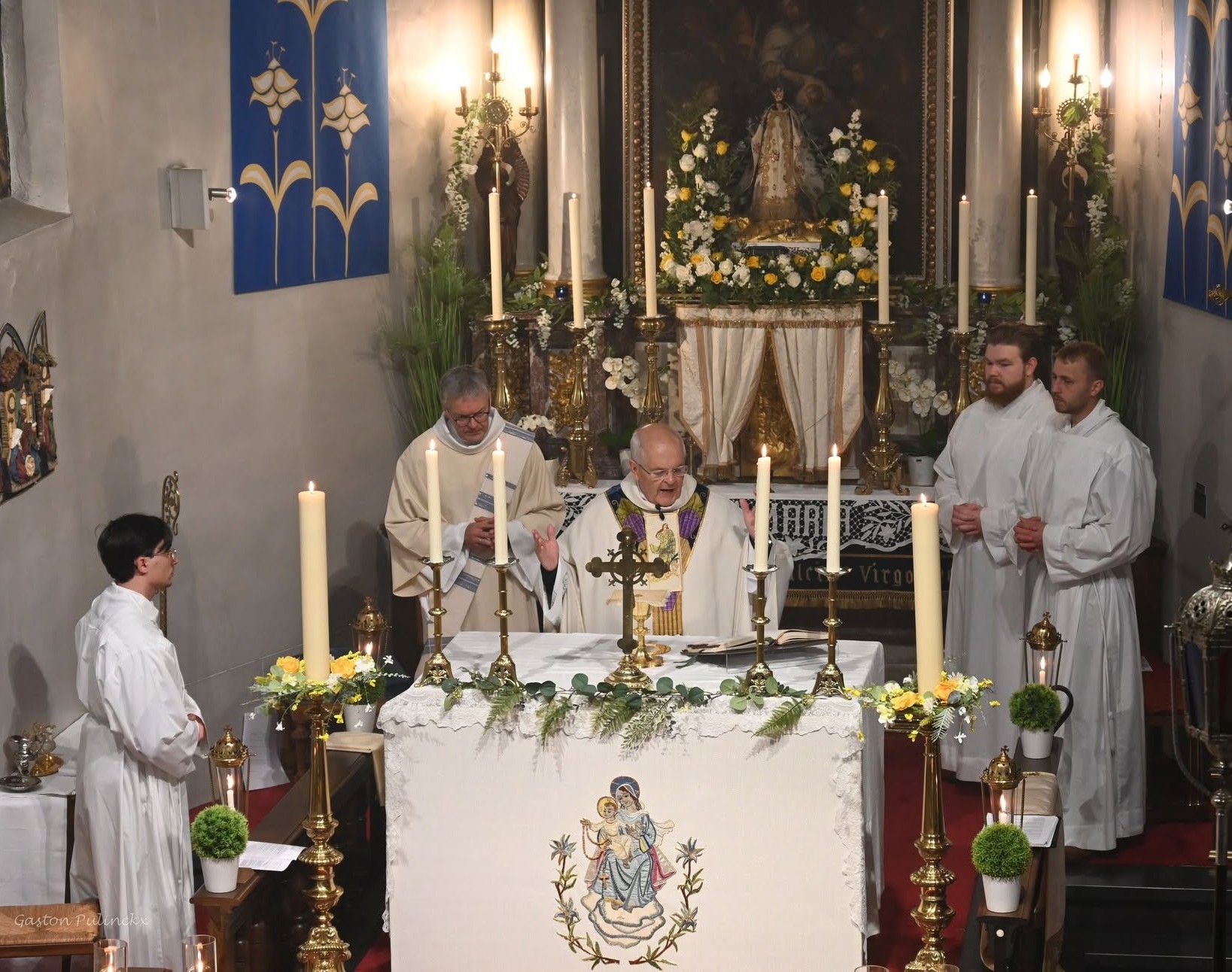 Eucharistieviering (mis) aan een altaar met kaarsen, een priester en misdienaars in een kerk of kapel.