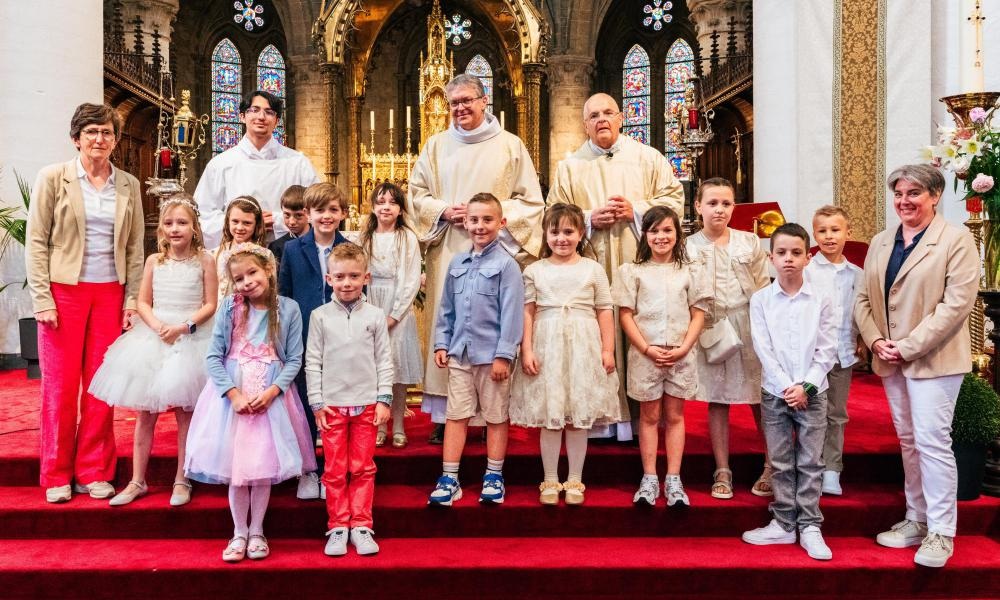 Eerste communie 2026 Een groep kinderen in feestelijke kleding samen met priesters en begeleiders tijdens een eerste communieviering.