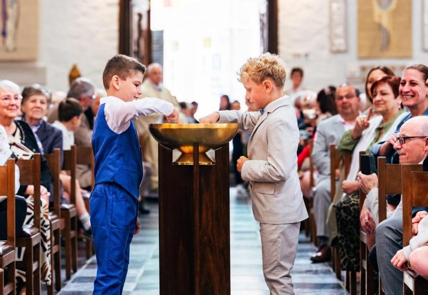 Eerste communie 2026 Twee jonge kinderen die bij een doopvont in een kerk staan, tijdens de religieuze plechtigheid : eerste communie.
