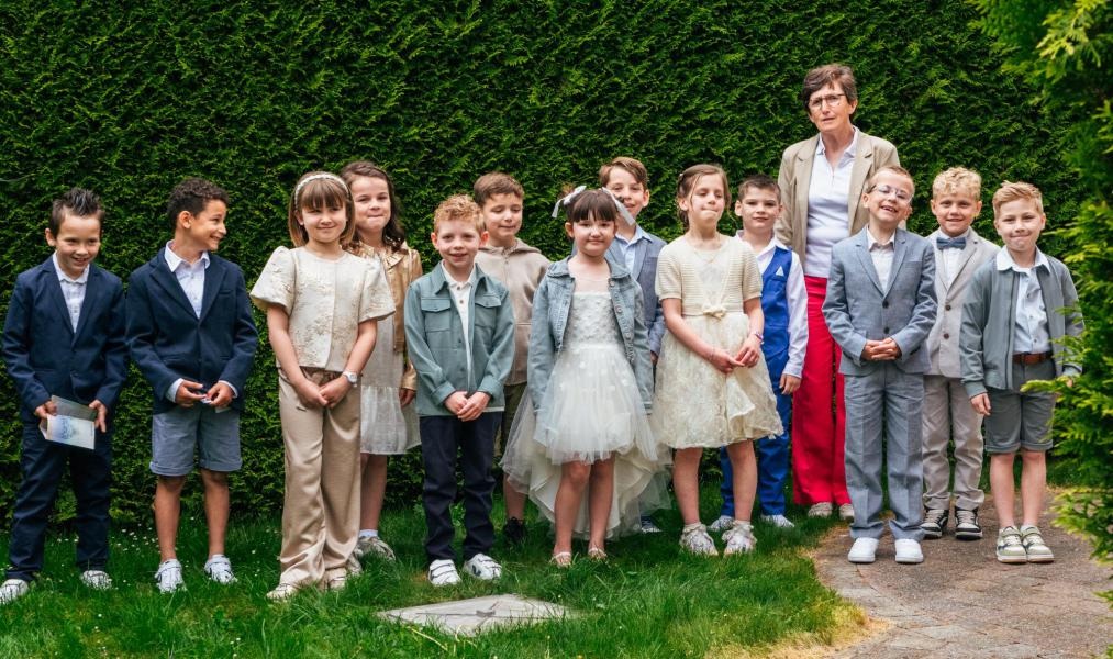 Eerste communie 2026 Een groep kinderen die deelnemen aan een eerste communieviering in een groene buitenomgeving.