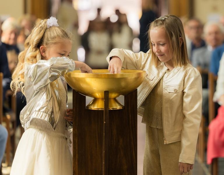 Eerste communie 2026 Twee kinderen bij een doopvont tijdens een religieuze viering: eerste communie.