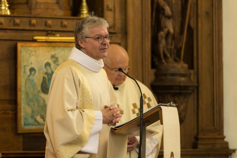 Eerste communie 2026 Diaken Luc in een liturgisch gewaad (een albe met een lichte albe/kazuifel of koorkap/stola) die tijdens een kerkelijke viering spreekt bij een ambo, in Zoutleeuw tijdens een plechtigheid: eerste communie.