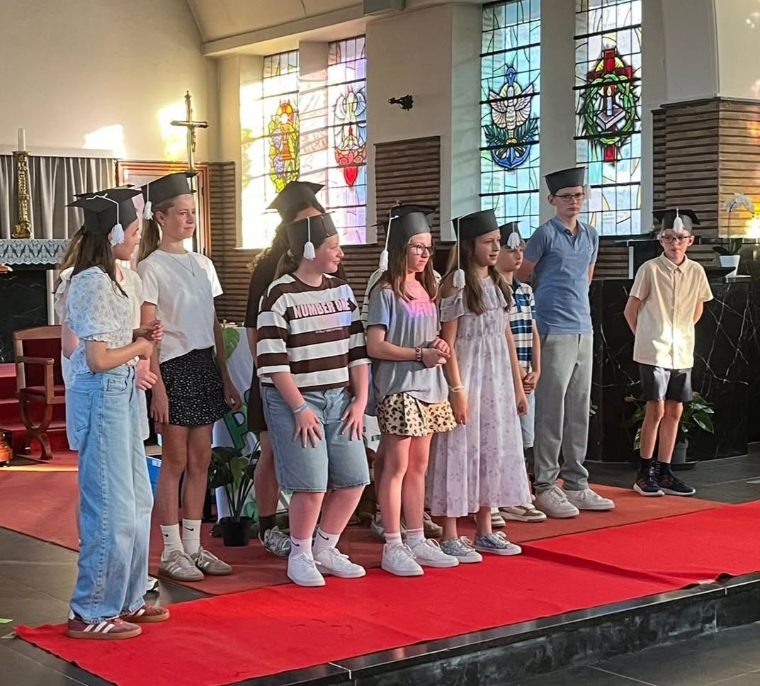 Proclamaties leerlingen in koele kerken Een groep kinderen (leerlingen uit het zesde leerjaar of vormelingen) die op een rood loperpodium in een kerk of school staan voor een plechtig afscheid of viering.
