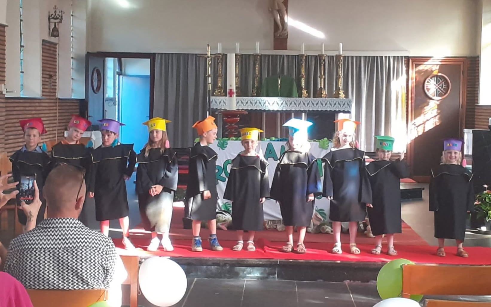 Proclamaties leerlingen in koele kerken Een schoolevenement of proclamatie (zoals een afscheid van de kleuters) waarbij kinderen in toga's en afstudeerhoeden op een podium staan.