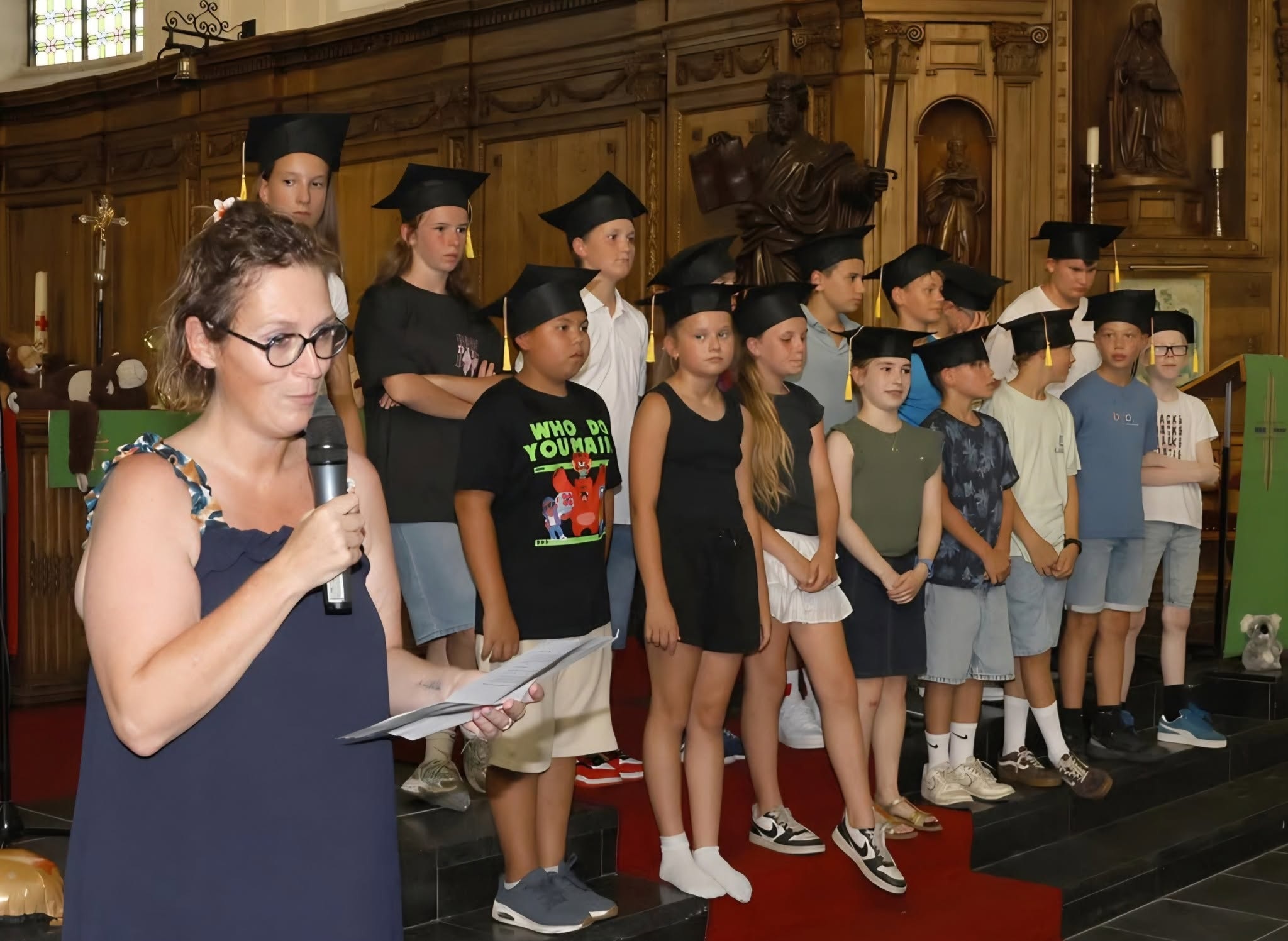 Proclamaties leerlingen in koele kerken Een schoolevenement of proclamatie (zoals een afscheid van het zesde leerjaar) in een kerk, waarbij leerlingen met een afstudeerhoedje op een podium staan naast een leerkracht met een microfoon.