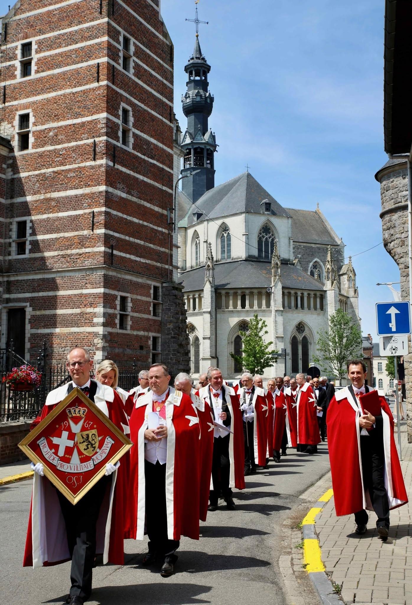 Een groep mensen in rode mantels en zwarte hoeden die deelnemen aan een religieuze of traditionele stoet (processie) in Zoutleeuw, met op de achtergrond een historische kerk.