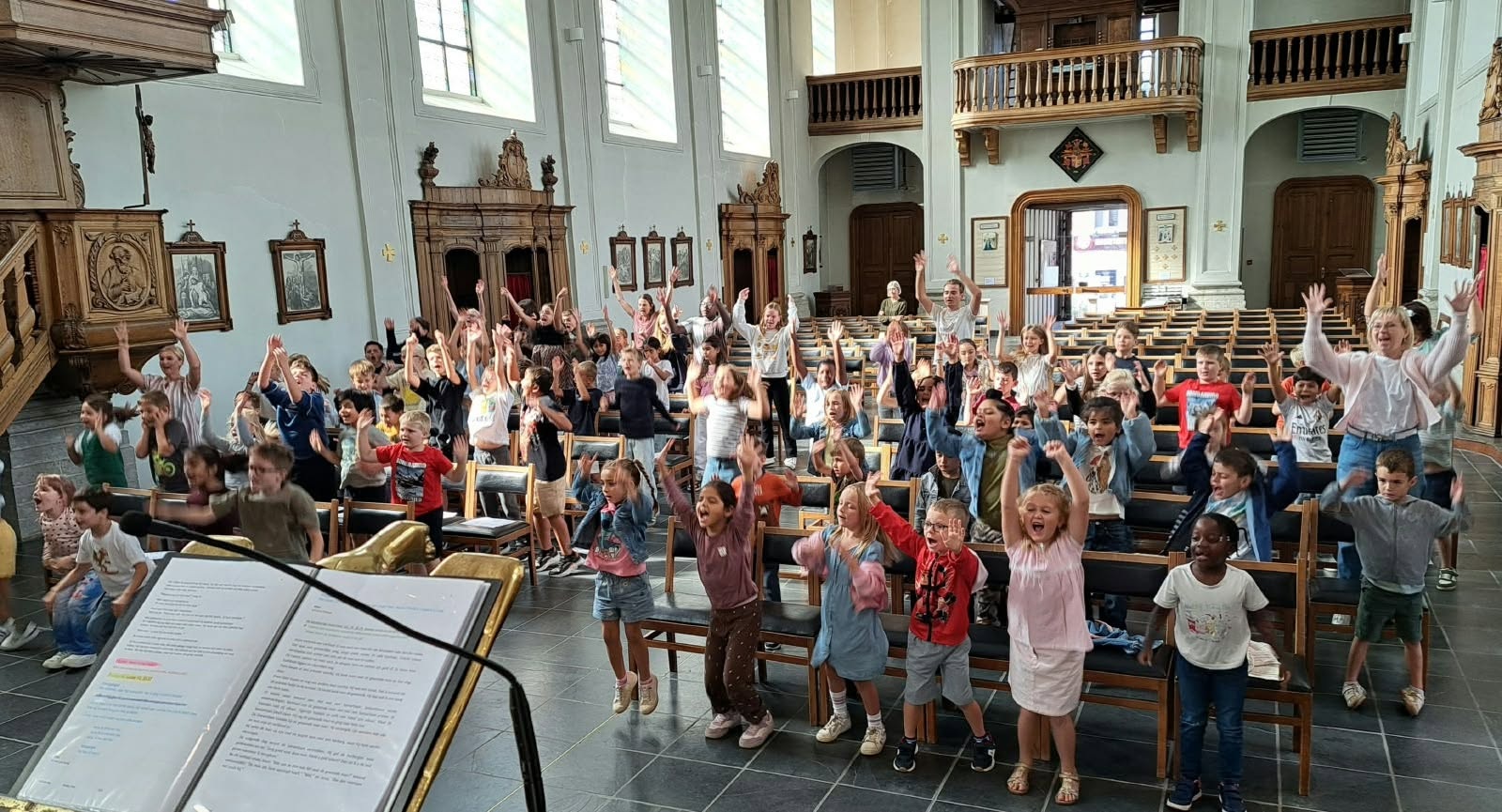 Een groep kinderen die enthousiast hun handen in de lucht steken in een kerk.