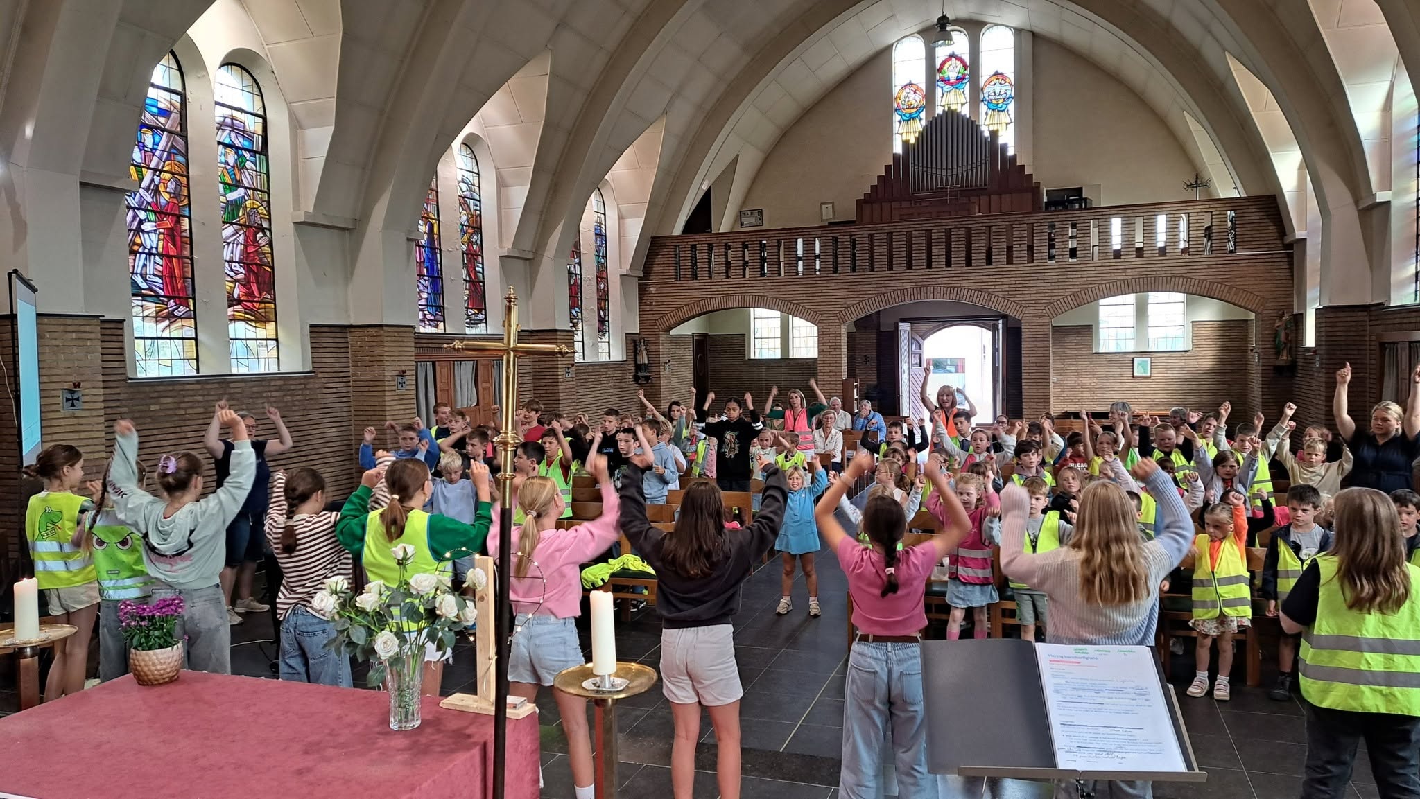 Een startviering of schoolviering in een kerk te tonen, met kinderen en begeleiders die hand in hand of met de handen in de lucht staan.