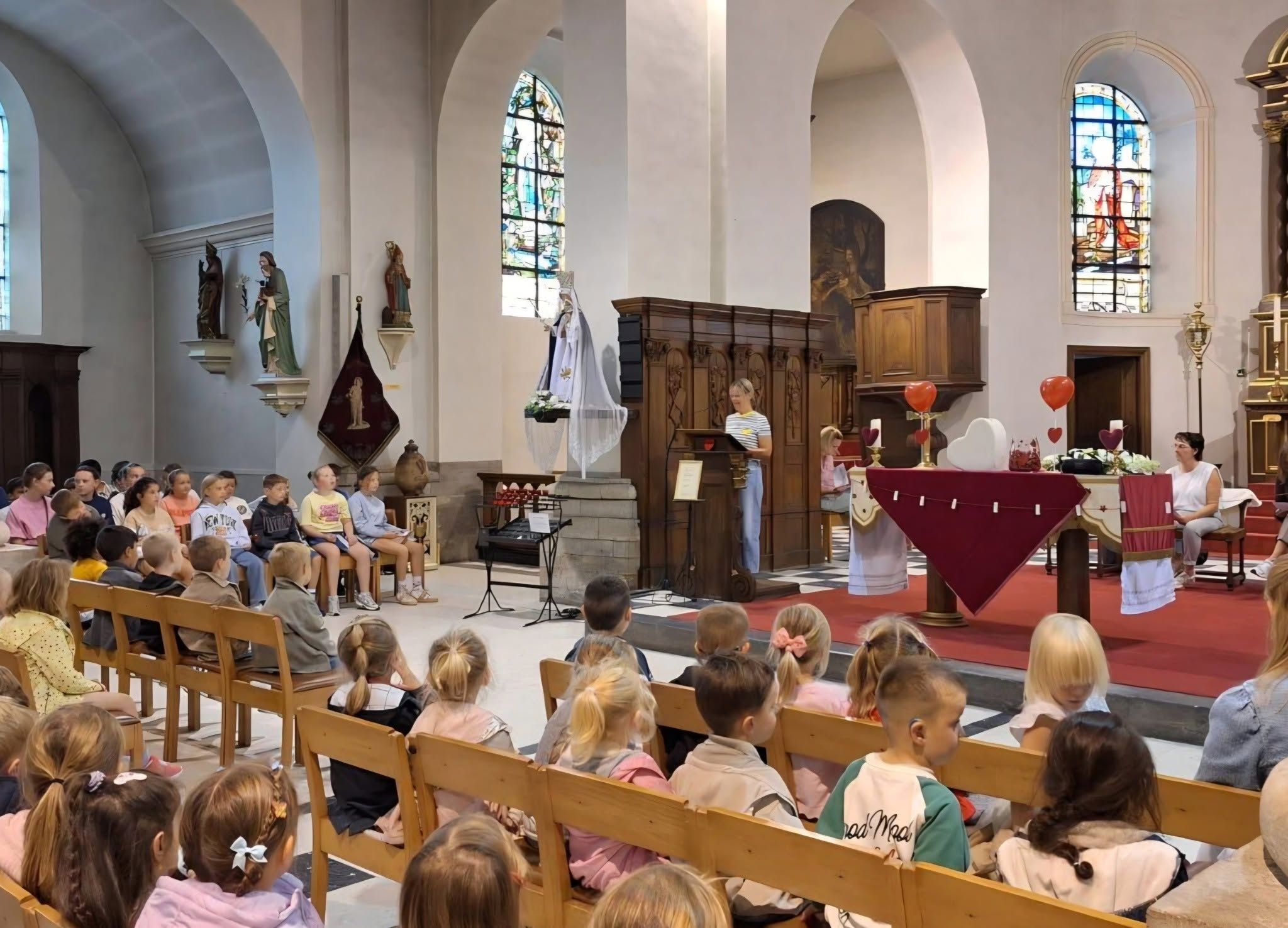 Het interieur van een kerk tijdens een viering met kerkgangers en een persoon bij een spreekgestoelte.