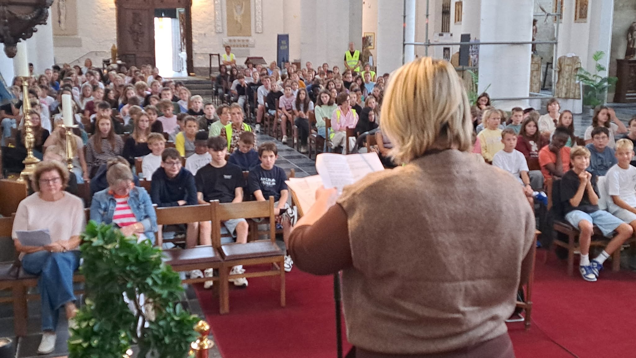 Middelbare scholen Zoutleeuw maken een gelovige start Viering met een volle kerk en iemand die vooraan bij een lezenaar staat te spreken of voor te lezen.