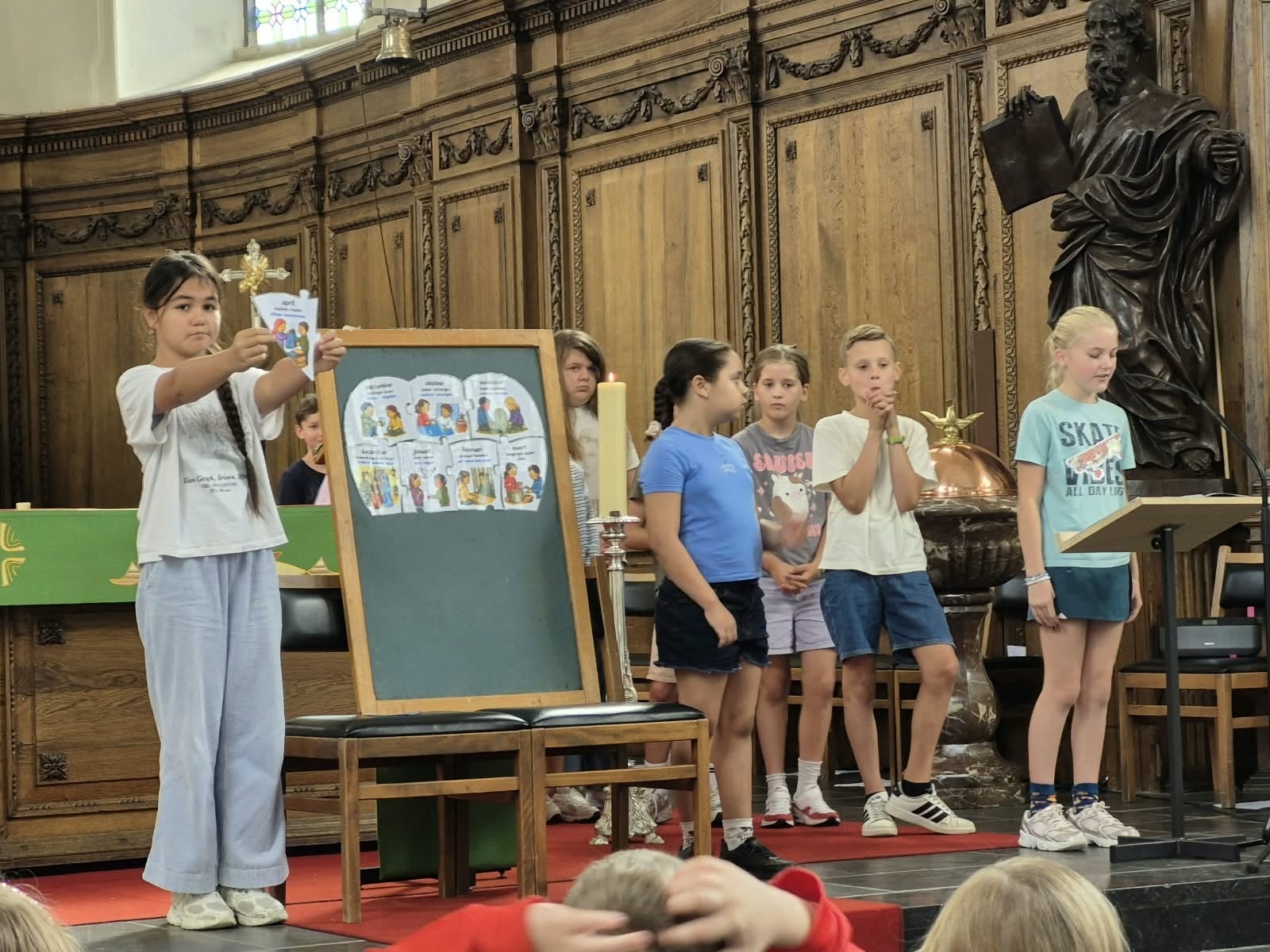 Een groep kinderen die voor in een kerk staan bij een schoolviering.