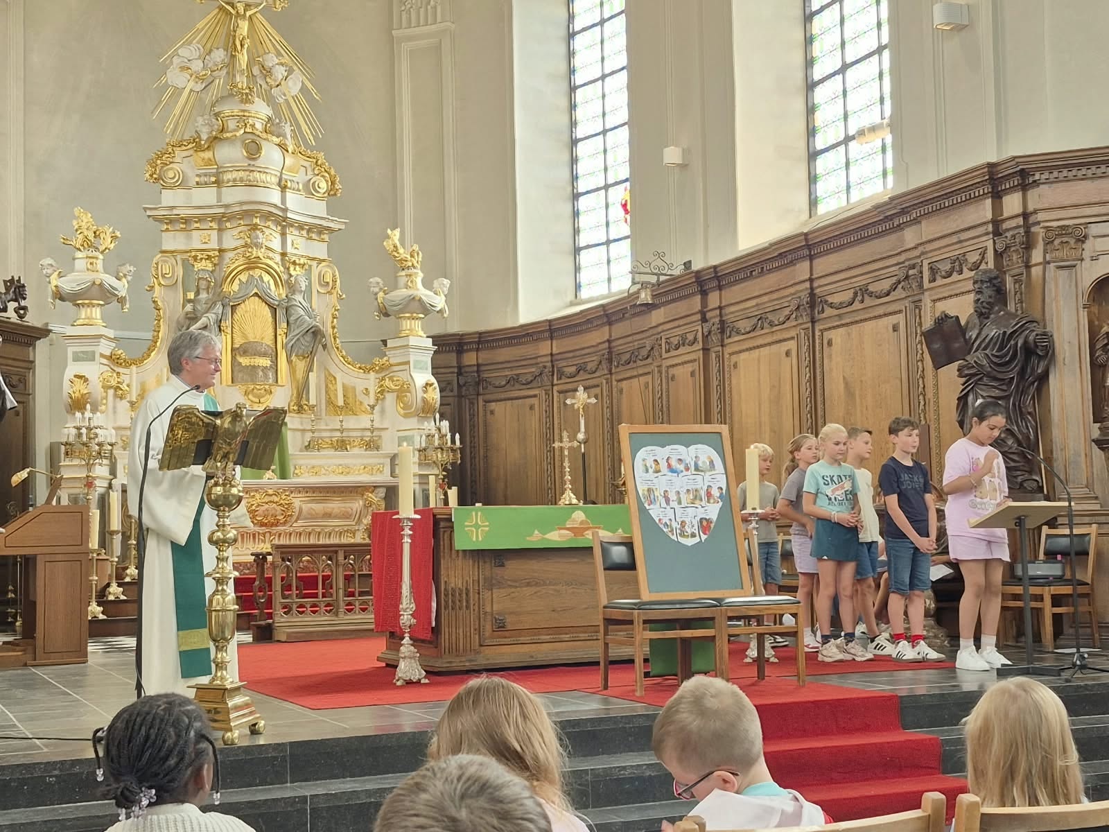 een eucharistieviering waarbij kinderen voor het altaar staan en een diaken spreekt vanaf een ambo of lessenaar.