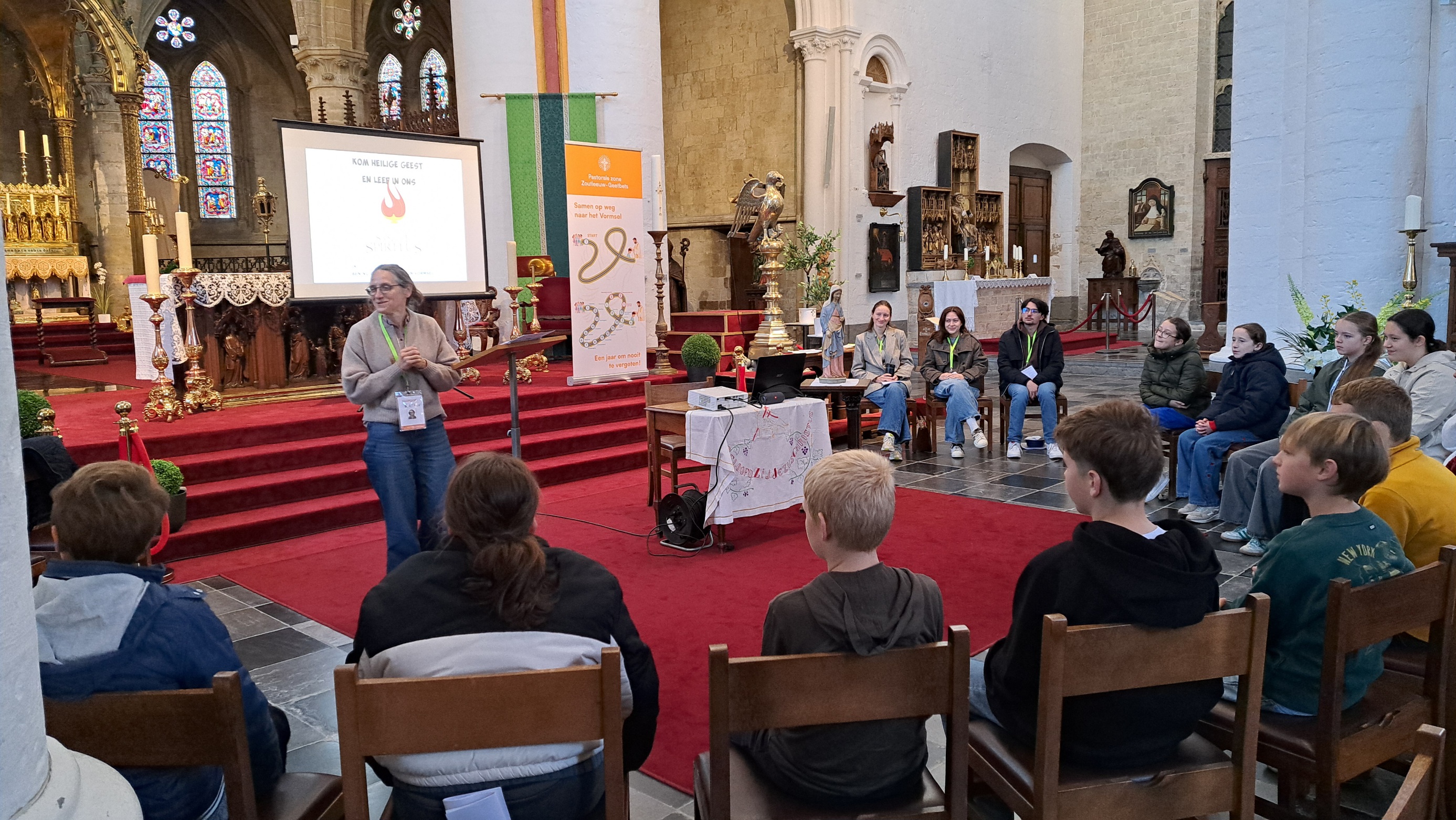 Samen op weg naar het vormsel Een bijeenkomst of infovergadering in een kerk, waarbij een spreker voor een groep jongeren staat in het kader van vormselvoorbereiding.