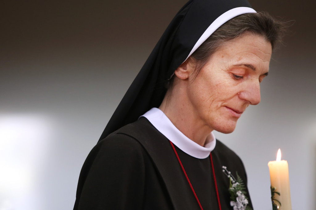 Zuster Bettina Berens tijdens haar professie. Bettina Berens in zwarte liturgische kledij en met kaars in de hand, tijdens haar professie.