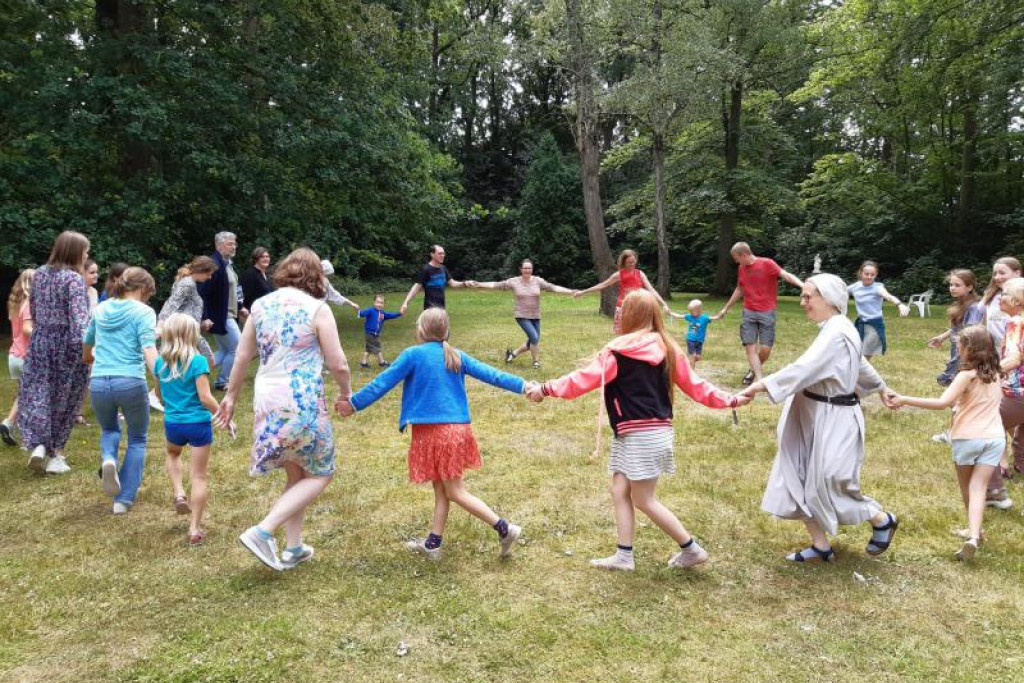 Plezier en bezinning voor het hele gezin op de vakanties van GezinStop bij de benedictinessen in Loppem. Ouders, kinderen en een zuster benedictines dansen in het rond. Foto van GezinStop-vakantie 2022.