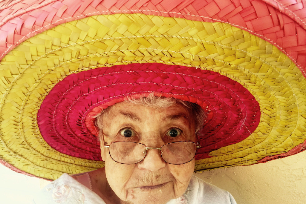Oud vrouwtje kijkt ondeugend in de lens, met kleurige sombrero op het hoofd