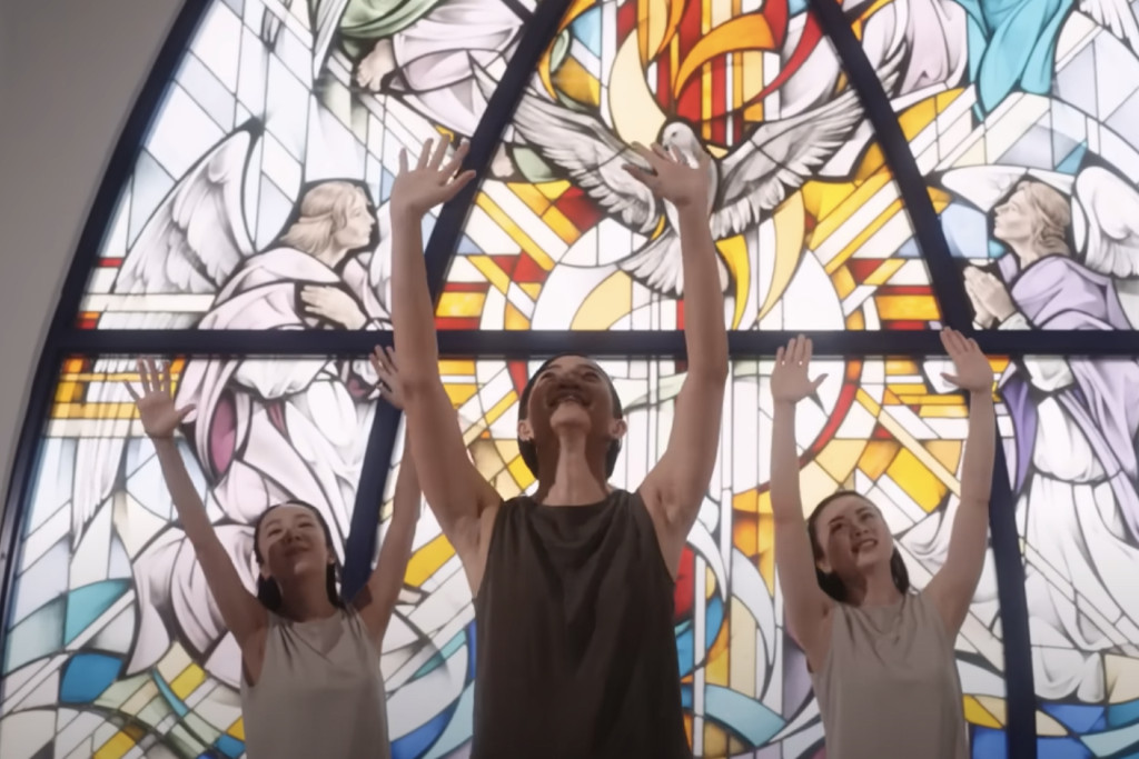 Schermafbeelding uit de clip: jonge dansers tegen licht van glasraam in een kerk.