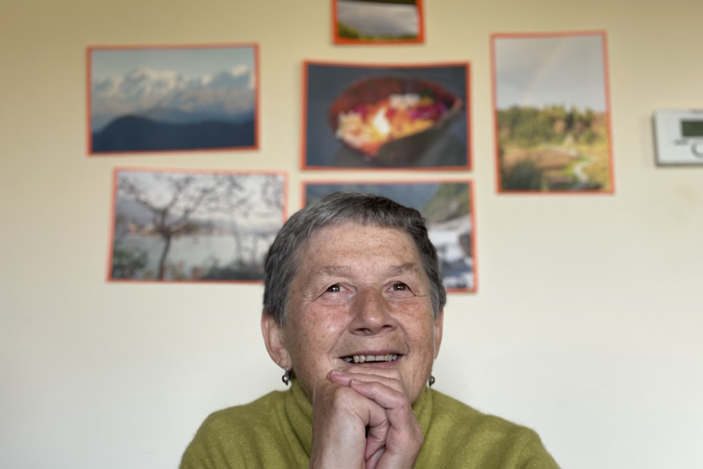 Sonja Van De Vijver kijkt dromerig omhoog. Achter haar hangen geprinte foto's van haar reizen naar India aan de muur.