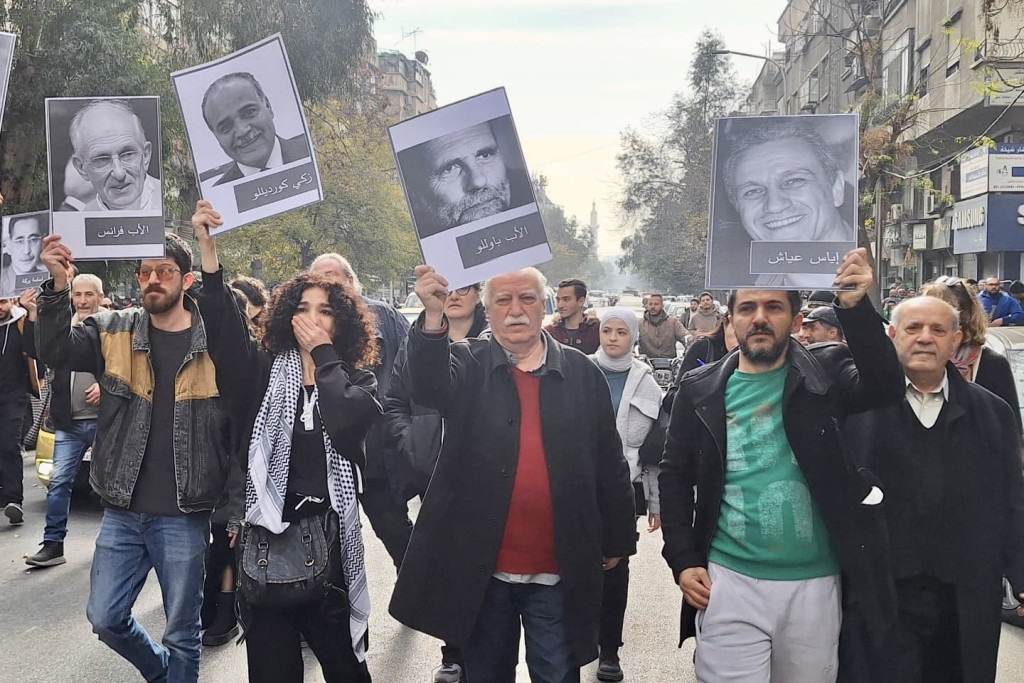 Betogers in Damascus steken portretten van vermisten in de lucht. In het midden een foto van Paolo Dall'Oglio.