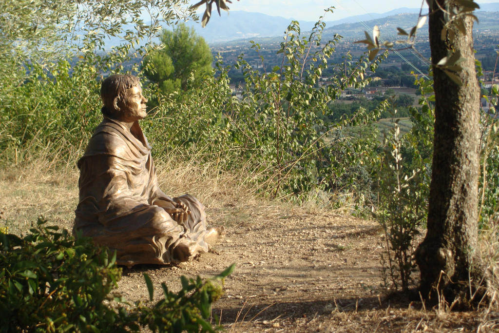 Beeld van Franciscus van Assisi in kleermakerszit uitkijkend over het landschap van op een berg.