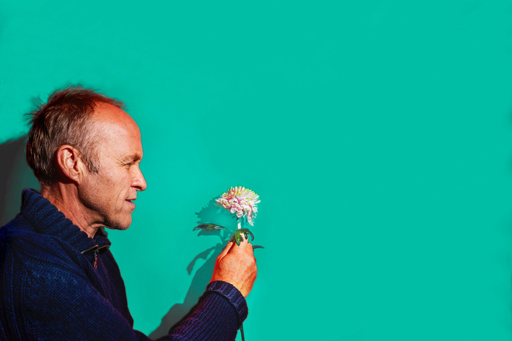Stef Bos met bloemetje in de hand tegen effen groene achtergrond