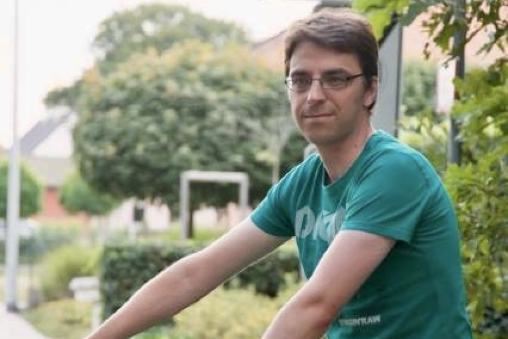 Diaken Jurgen Deckx (43) op de fiets bij een bord met plaatsnaam Heide Dessel.