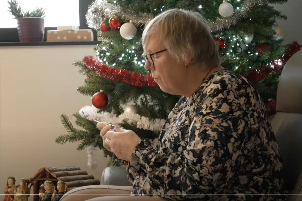 Dame haakt engeltjes bij kerstboom.