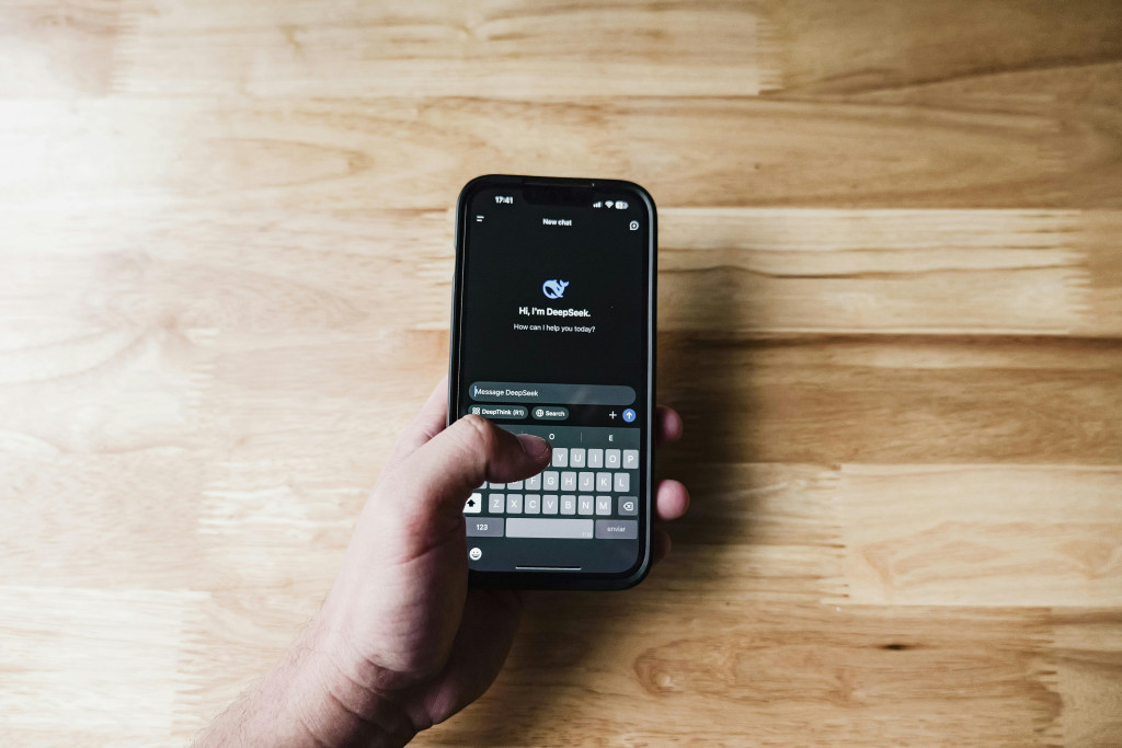 hand met mobiele telefoon waarop de chatbox DeepSeek wordt geopend.