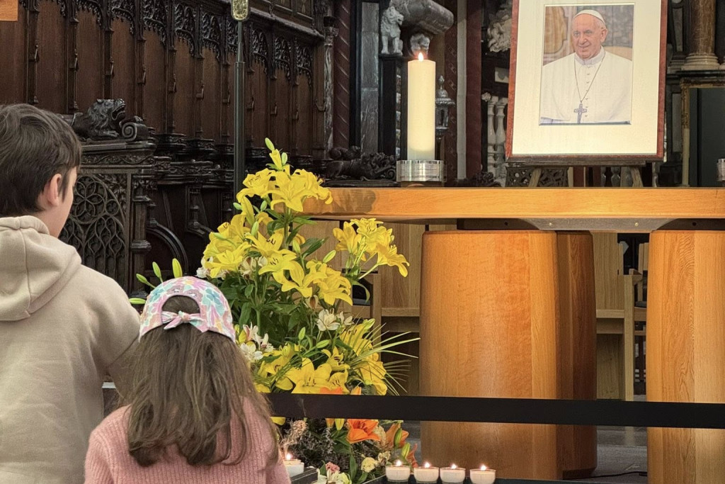 Een foto van paus Franciscus op het altaar van de Sint-Salvatorkathedraal in Brugge. Twee kinderen steken er een kaarsje bij aan.