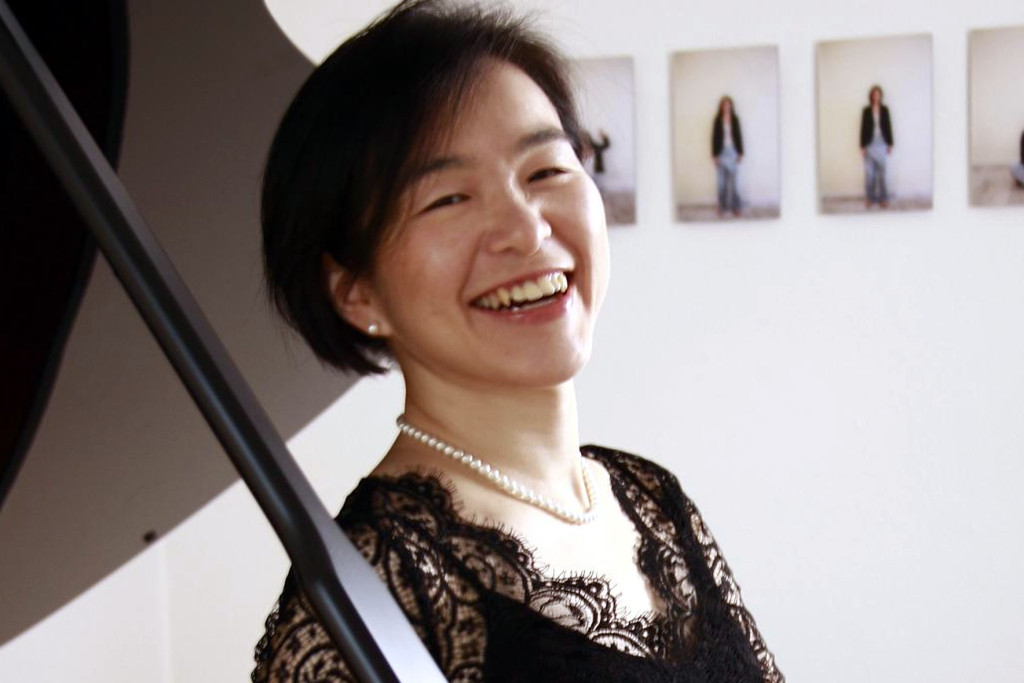 Joanna Jimin Lee, de zuster die ook concertpianiste is. Joanna Jimin Lee in concertkledij bij de piano, brede glimlach