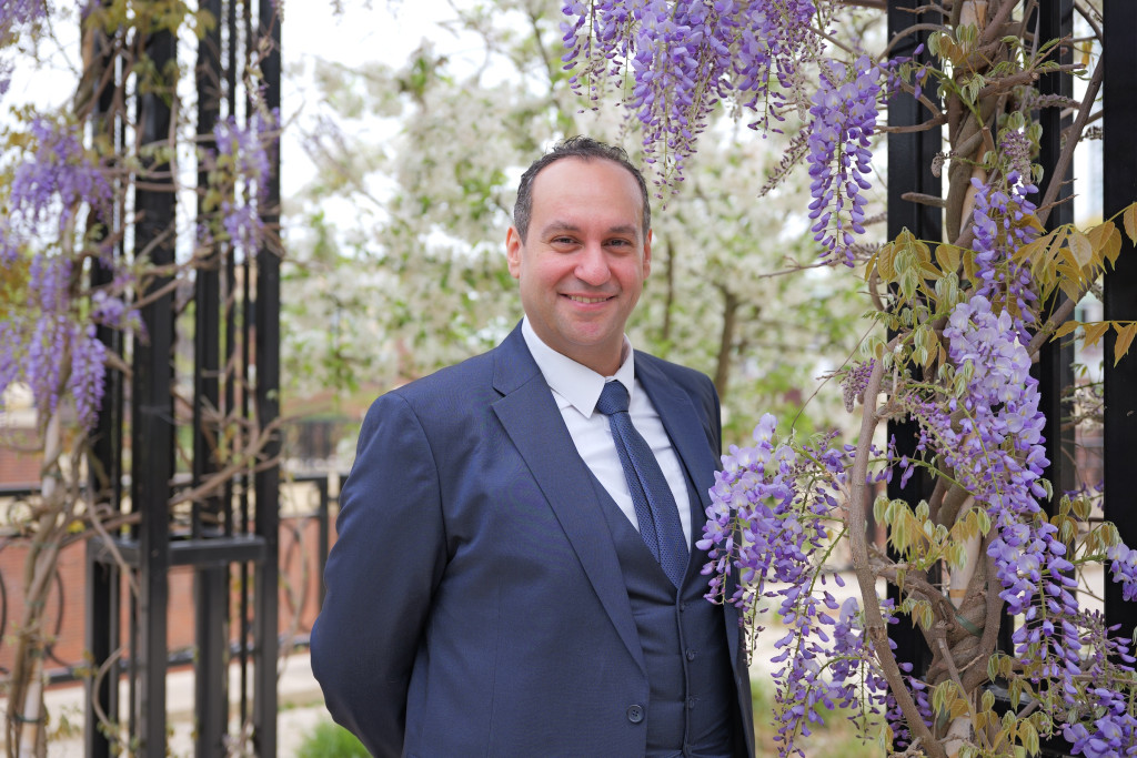Joseph Shenouda poseert tussen de bloemen van een blauwe regen.