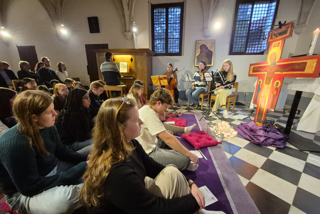 Jongeren in de dekenale kerk in Aalst, op de grond gezeten bij een kruis en talrijke kaarsjes voor het Taizégebed.