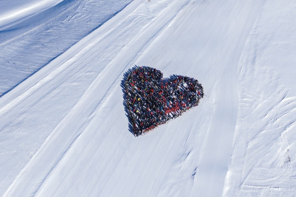 Mensen staan in groep bijeen in de contouren van een hart, van bovenaf gefotografeerd op de sneeuwpiste.