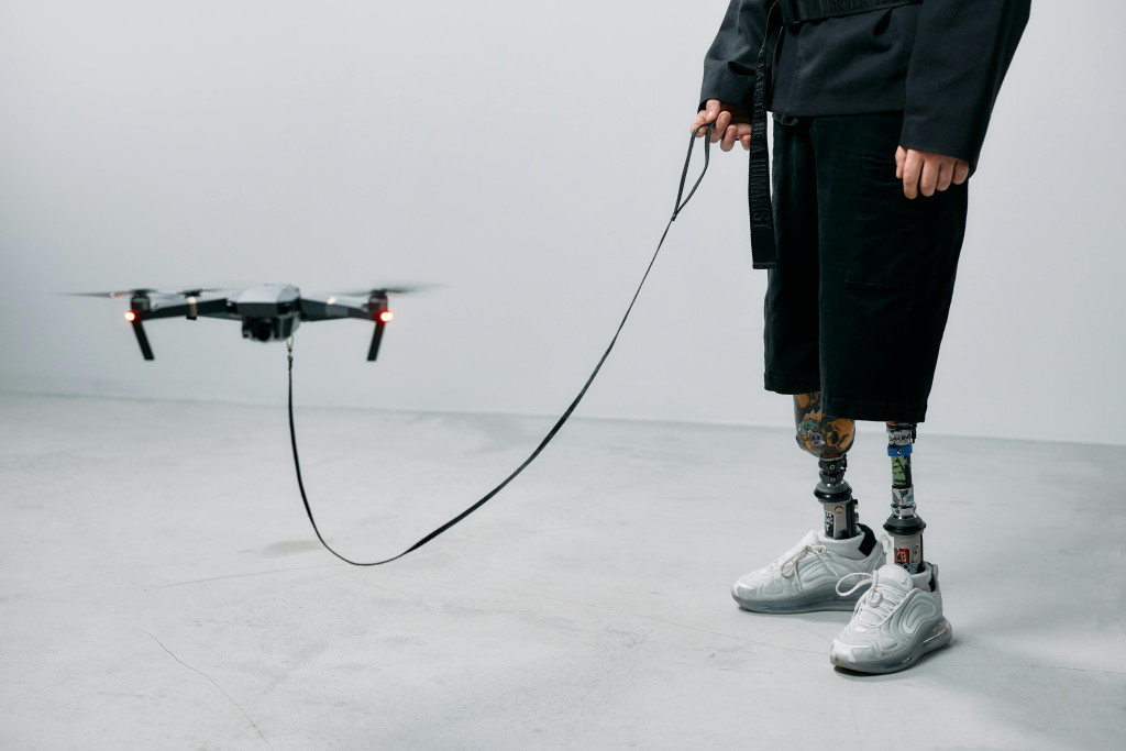 Vrouw met robotbenen houdt een drone aan de leiband alsof het een hondje is.