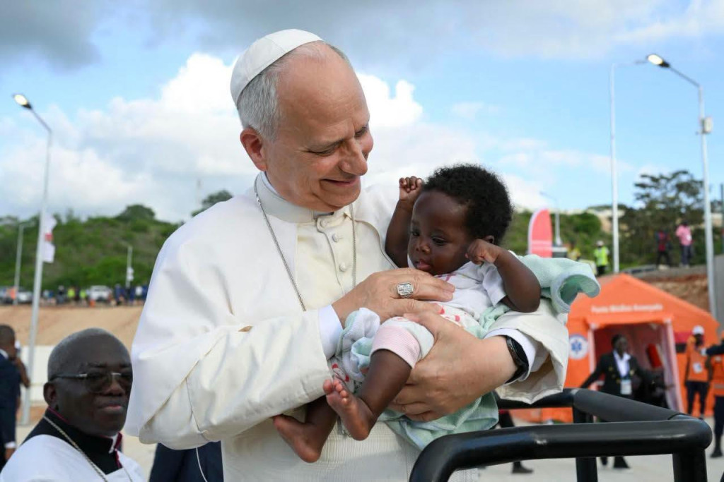 Met een baby in de armen heeft paus Leo nog meer een (groot)vaderlijke uitstraling. Paus Leo kijkt vertedert naar een baby op zijn arm, na het rozenkransgebed bij het mariaoord Mama Muxima in Angola.