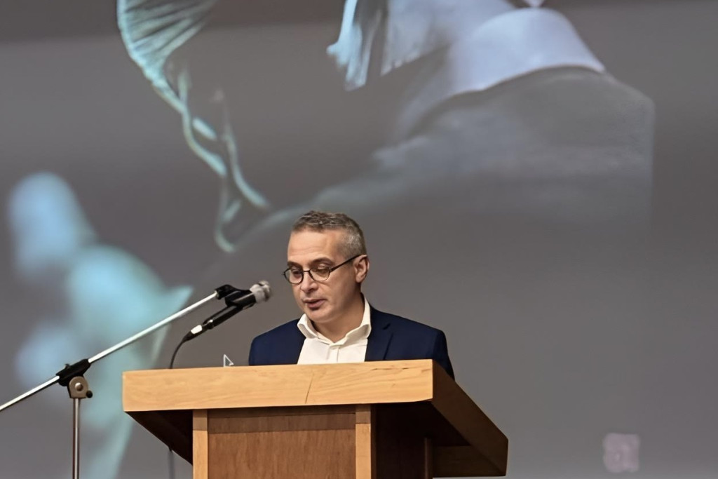 Bahattin Koçak: 'Er zijn momenten waarop geloof niet vanzelfsprekend voelt. Niet zozeer omdat je God verliest, maar omdat je vertrouwen in mensen wankelt.' Bahattin Koçak aan de micro met achter hem een geprojecteerd beeld van een moslim in gebed.