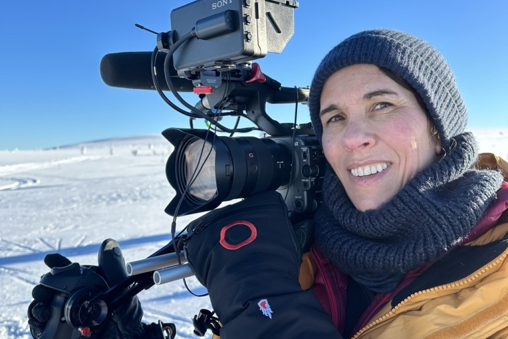 Kristel Waterloos met zware camera op de schouder en dik ingeduffeld, op reportage in het Hoge Noorden.